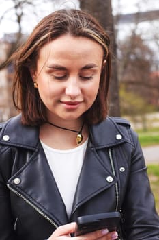 Pretty girl sitting in a city park on a bench with a phone, dialing a number. High quality photo