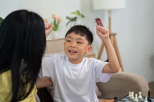 A mother and son cheering together after finishing a chess game, showcasing excitement and bonding at home.