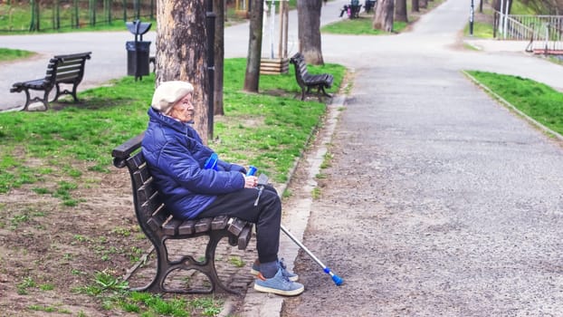 Poland, Wroclaw, April 13, 2025. A lonely old woman pensioner with a cane sits on a bench in the park. High quality photo