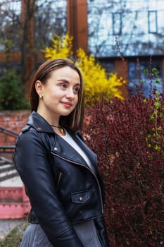 Girl in a black jacket near ornamental bushes in spring. High quality photo