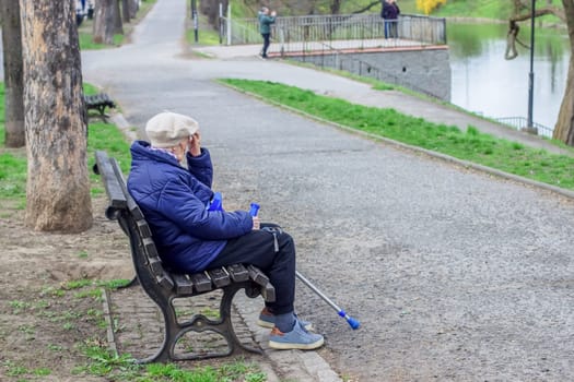Poland, Wroclaw, April 13, 2025. A lonely old woman pensioner with a cane sits on a bench in the park. High quality photo