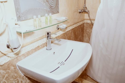 Hotel bathroom with mirror and disinfected sink sign. Washing accessories in hotel bathroom. Shampoo and gel in small bottles on shelf.