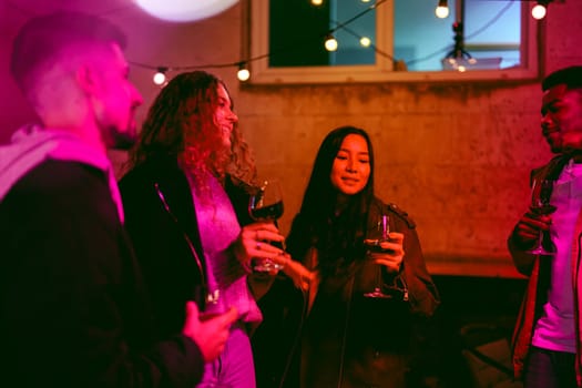 Group of friends gathered outside in the evening, sharing drinks and laughter. Colorful lights create a vibrant atmosphere as they enjoy each other's company.