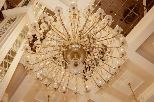 Huge, luxurious crystal chandelier with gold elements and hanging glass pendants, round shape. bottom view, ceiling with mirror elements. luxury furnishings