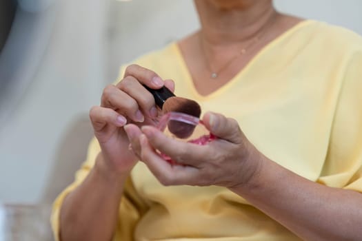 A mature woman prepares her makeup using a brush, emphasizing her beauty routine and the joy of self-expression at any age.