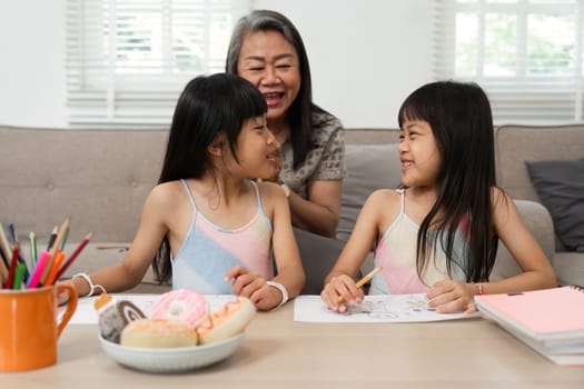 A joyful grandmother shares quality time with her twin granddaughters as they enjoy drawing and learning together, fostering creativity and connection.