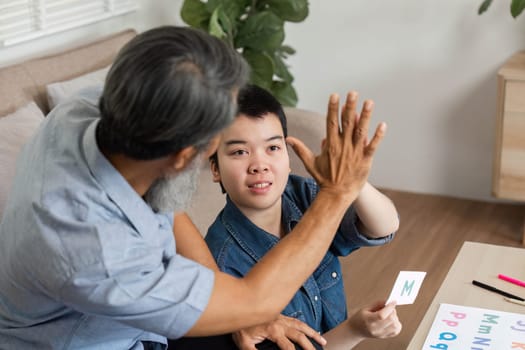 A caring grandfather is engaged in a fun learning session with his grandchild, who has Down syndrome, using letters and cards to enhance communication skills.