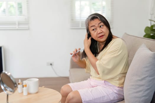 A mature woman brushes her hair while seated comfortably, embracing her beauty routine and showcasing age diversity in personal care.