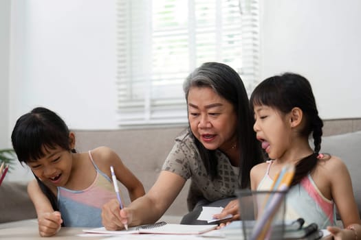 A caring grandmother helps her granddaughters with their drawing, promoting creativity and learning in a nurturing environment.
