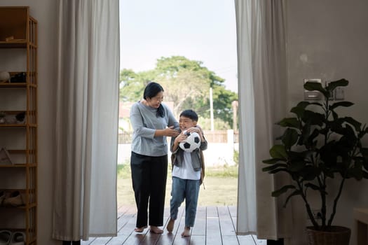A mother assists her son with a soccer ball, preparing for a fun outdoor play session, showcasing their loving relationship and active lifestyle.