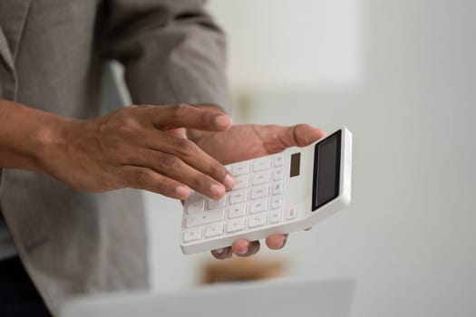 A man operates a calculator while discussing financial details, highlighting the analytical aspect of their business meeting.