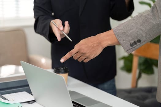 In a collaborative setting, two men point at a laptop screen, emphasizing key points while discussing project details and strategies.