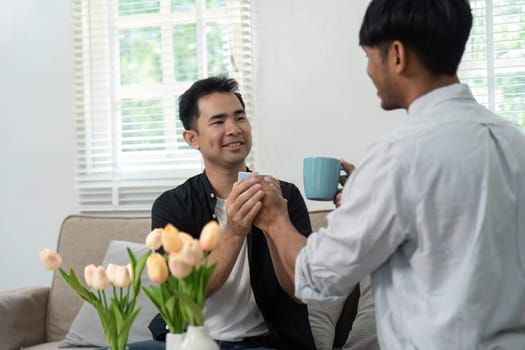 A couple shares a tender moment, exchanging coffee cups and smiles. Their interaction highlights the simple joys of everyday life in an LGBT relationship, emphasizing love and connection.
