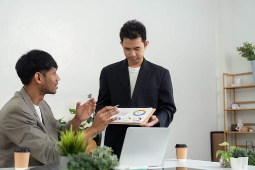 In a modern office, one professional presents a data analysis report while the other listens attentively, showcasing teamwork and strategic planning.