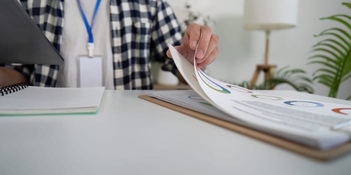 A young Asian man reviewing documents on a tablet while seated at a modern home office desk, promoting a healthy work-life balance in a vibrant environment.