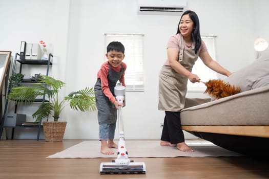 A cheerful mother watches her son vacuum the living room floor, highlighting the importance of teamwork in household chores.