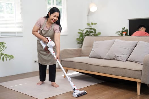A dedicated woman is actively vacuuming her living room, showcasing her commitment to maintaining a clean and tidy home environment.