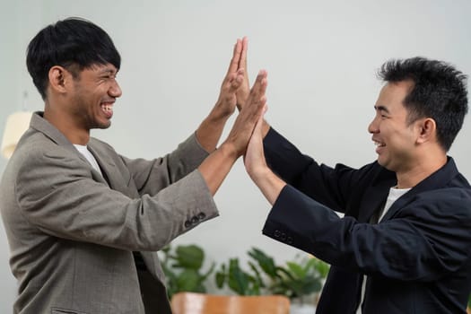 Two business partners express their excitement with a high-five, showcasing a positive work environment and camaraderie.