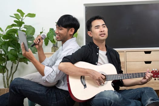 A couple sits back-to-back, one playing guitar and the other singing into a microphone. Their musical interaction illustrates the joy of creativity and shared passions in an LGBT relationship.