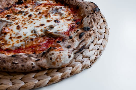 Delicious wood fired pizza with melty cheese and toppings on woven mat.