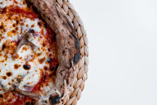 Close up of wood fired pizza with cheese and tomato on woven mat.
