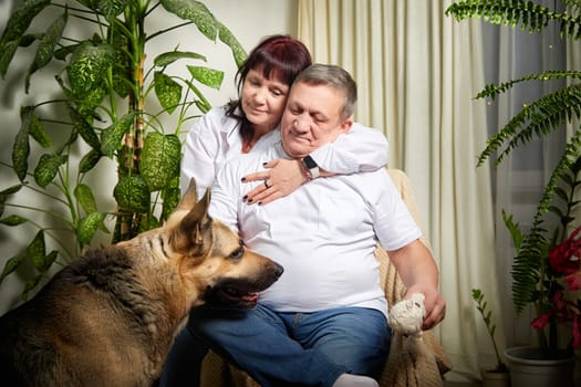 A couple enjoys a warm embrace while their german shepherd sits nearby, showcasing family love in their inviting home.