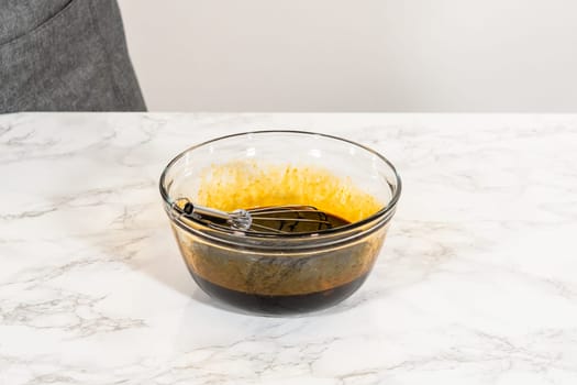 A close-up view of a glass bowl containing molasses and two large eggs for Spiced Gingerbread Cookie Dough Perfect for Baking. The dark molasses contrasts with the bright egg yolks, ready to be blended.