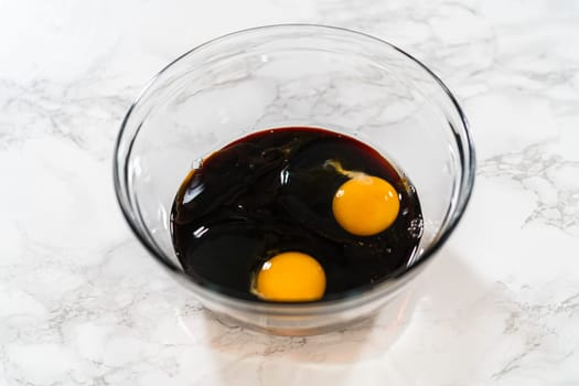 A top-down view of dark molasses and two eggs in a glass bowl, part of the wet ingredients for Zesty Orange Gingerbread Cookie Dough. The molasses adds depth and a rich color to the gingerbread.