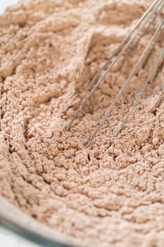 Mixing dry ingredients for Chocolate Gingerbread Cookie Dough, including flour, cocoa powder, cinnamon, ground ginger, and cloves in a glass bowl. The ingredients are layered and ready to be combined, creating a rich, aromatic base for the cookie dough.