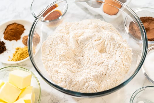Organized setup of ingredients for Pale Gingerbread Cookies with Subtle Spice Flavor. Central bowl with flour is surrounded by bowls with spices, butter, eggs, and maple syrup.