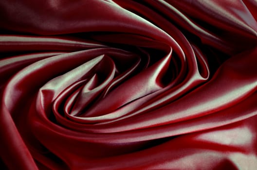Top view of polished dark red silk cloth with silky sheen and beautiful natural draping. Suitable for design and wallpaper background.