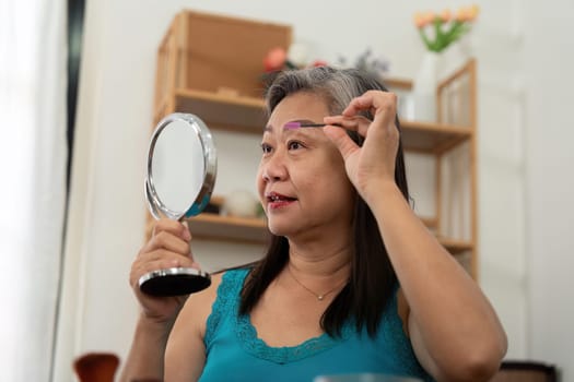 An elderly woman practicing wellness by grooming her appearance using a mirror at home, highlighting the importance of self-care and confidence.