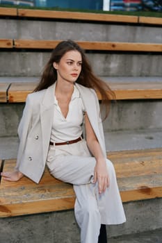 A businesswoman dressed in a chic outfit, showcasing poise and grace, seated on wooden steps in an urban setting, emphasizing professionalism and style.