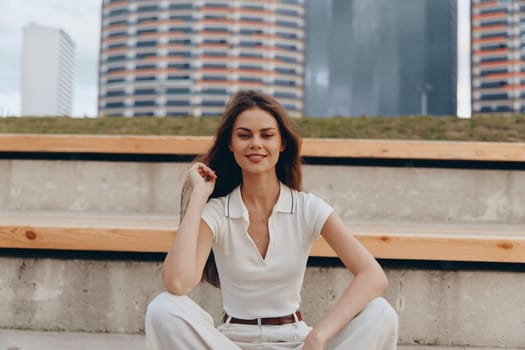 A self-assured woman in business wear smiles while sitting outdoors in a vibrant city environment, showcasing confidence and professionalism. The urban scene enhances her motivated expression and business-focused theme.