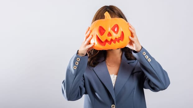 Young Asian female balancing an orange pumpkin with a cheerful smile, all amidst a backdrop of charming ghost pumpkins, creating a festive Halloween atmosphere. Halloween Day Concept