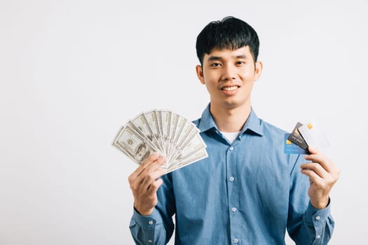 Portrait of a happy young man choosing to use dollars and a credit card for payment, showing his confidence. Studio shot isolated on white, highlighting financial decision-making.