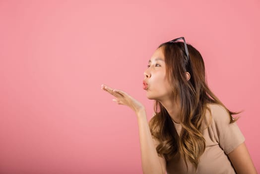 Asian happy portrait beautiful cute young woman teen standing blowing kiss air side something on palm hands expresses her love looking to camera studio shot isolated on pink background with copy space