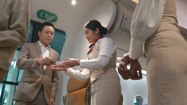 Asian flight attendants greeting welcoming passengers walking and coming on board in airplane, happy air stewardess or airhostess check passenger ticket boarding pass during trip travelling