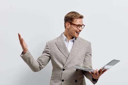 Smiling man in beige blazer interacts with laptop, using hand gestures while looking at device, conveying confidence and communication. Studio portrait emphasizing technology and professional mood.