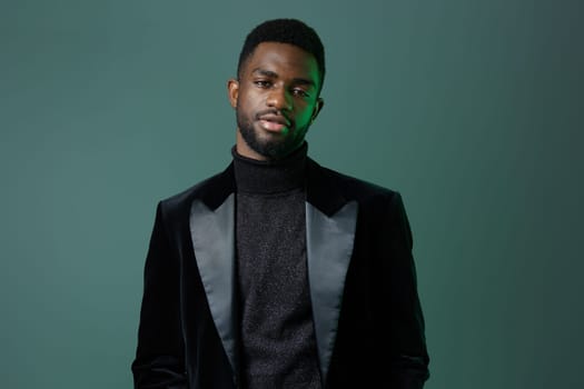 A confident businessman in a sleek black suit and turtleneck stands against a vibrant green background, exuding sophistication.