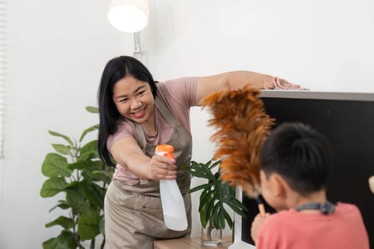 A child joyfully participates in home cleaning, using a feather duster on a TV, highlighting the importance of involving kids in household chores.