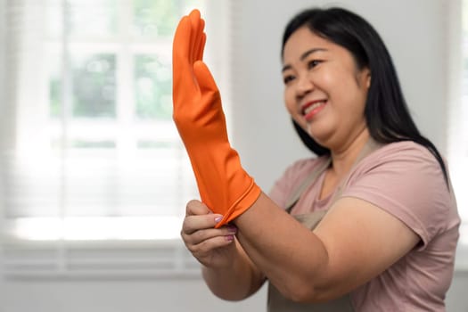 A woman is cheerfully putting on rubber gloves, ready to engage in cleaning tasks, showcasing a proactive approach to maintaining her living space.