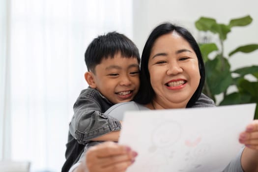 A mother joyfully holds her son as he shows off his colorful drawing, highlighting the bond they share through creativity and encouragement.