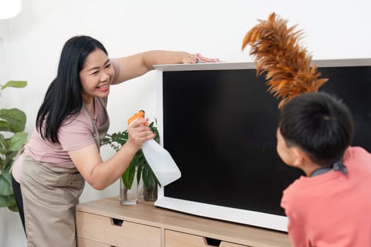 A joyful interaction between a woman and a child as they clean together, using a spray bottle and feather duster to make home cleaning a fun activity.