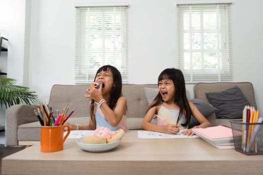 Two girls are immersed in their art projects, laughing and sharing snacks, creating a delightful atmosphere of creativity and joy in their home.