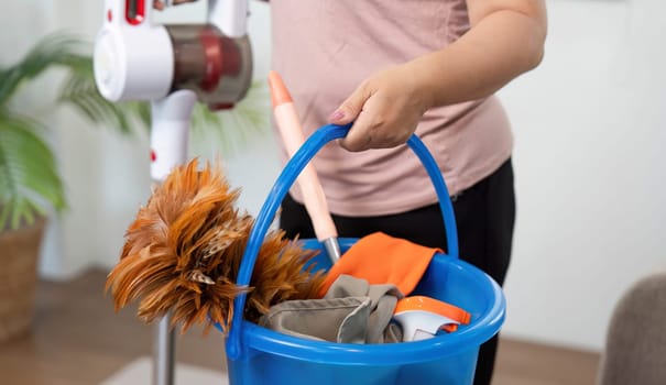 A woman is holding a blue bucket filled with cleaning supplies, demonstrating her readiness to tackle household chores with enthusiasm and efficiency.