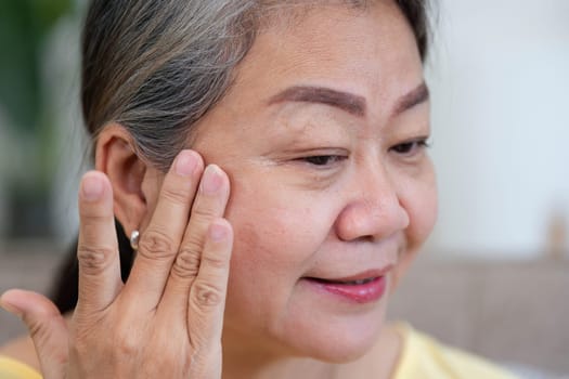 A mature woman smiles as she gently applies cream to her face, reflecting the joy of self-care and the beauty of aging gracefully.
