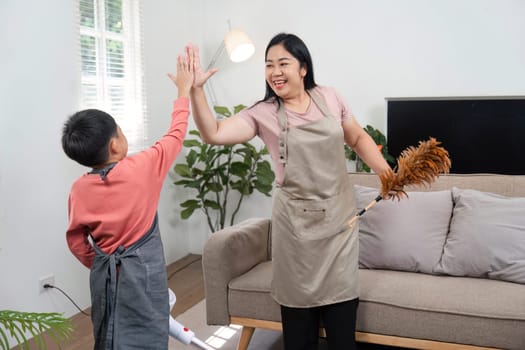A mother and her son high-five each other while engaging in a fun cleaning session at home, showcasing teamwork and family bonding.