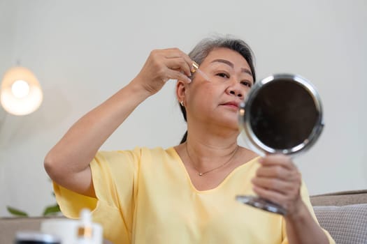 An older woman applies skincare serum while gazing into a mirror, emphasizing self-reflection and the beauty of aging gracefully.