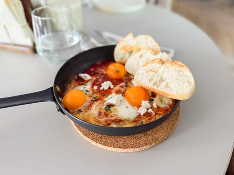 Shakshuka served hot in pan with bread slices. Comfort food, modern brunch and urban culinary style.
